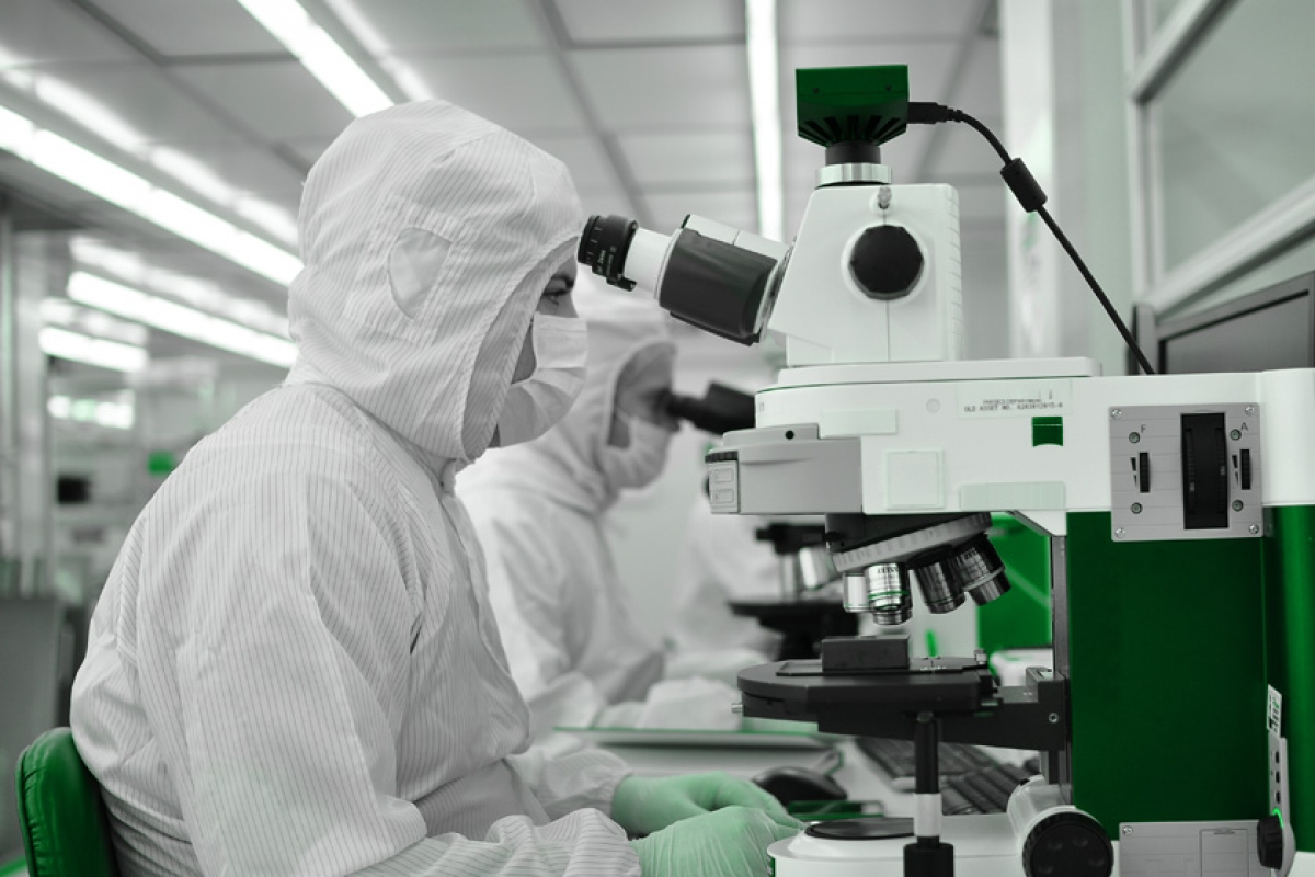 Specialist examining samples through a microscope in a cleanroom